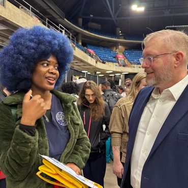 Two people engage in a lively conversation at a crowded indoor event.