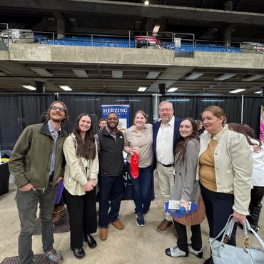 Group of seven people smiling at a Herzing University event indoors.