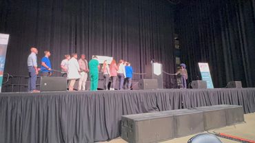 A group of people standing on stage holding a rope, with one person separated at the podium.