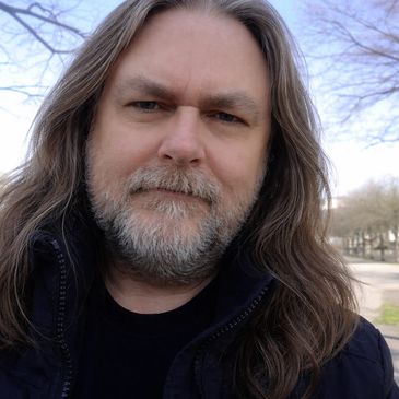 Man with long hair and beard outdoors on a clear day.
