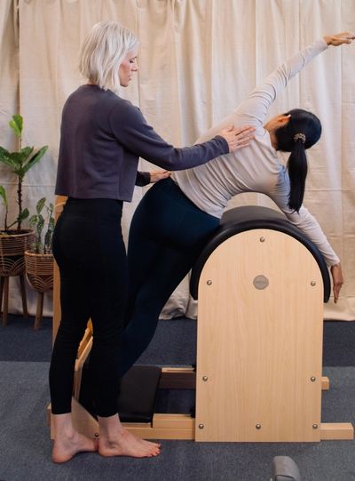 Instructor assisting a woman doing Pilates on equipment.