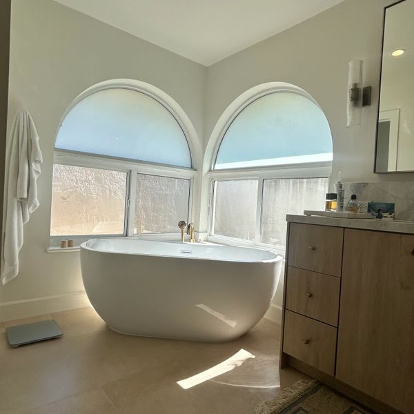 Modern bathroom with a freestanding tub and arched windows.