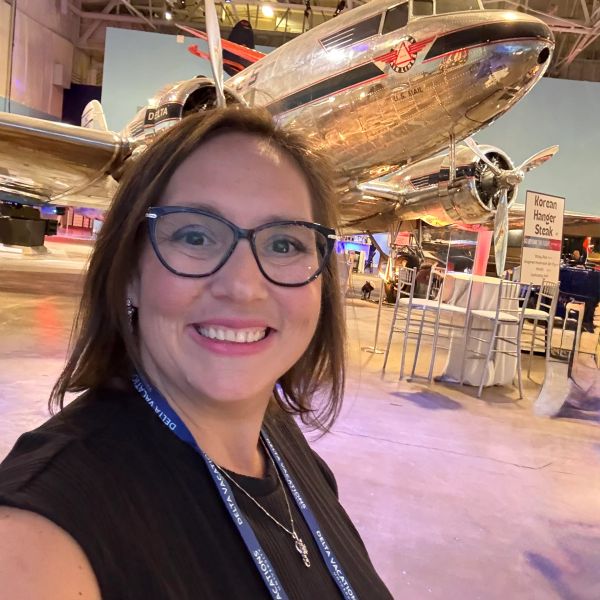 Smiling woman with glasses in an aircraft hangar with a vintage airplane.