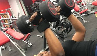 A person lifting dumbbells in a gym while wearing headphones and wrist straps.