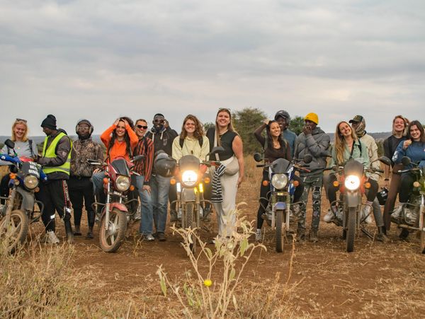 Group of young adults with motorcycles in an outdoor rural setting.