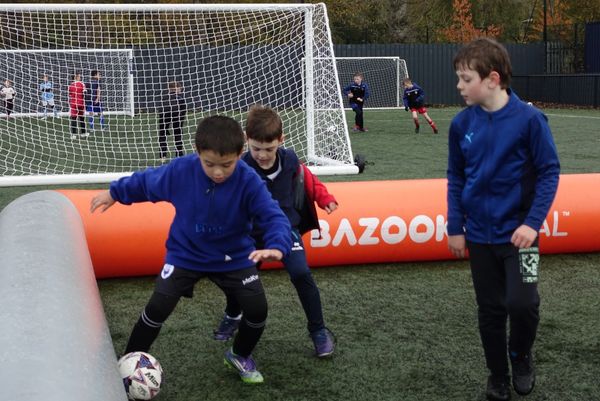 Children playing soccer on a field near a goal.