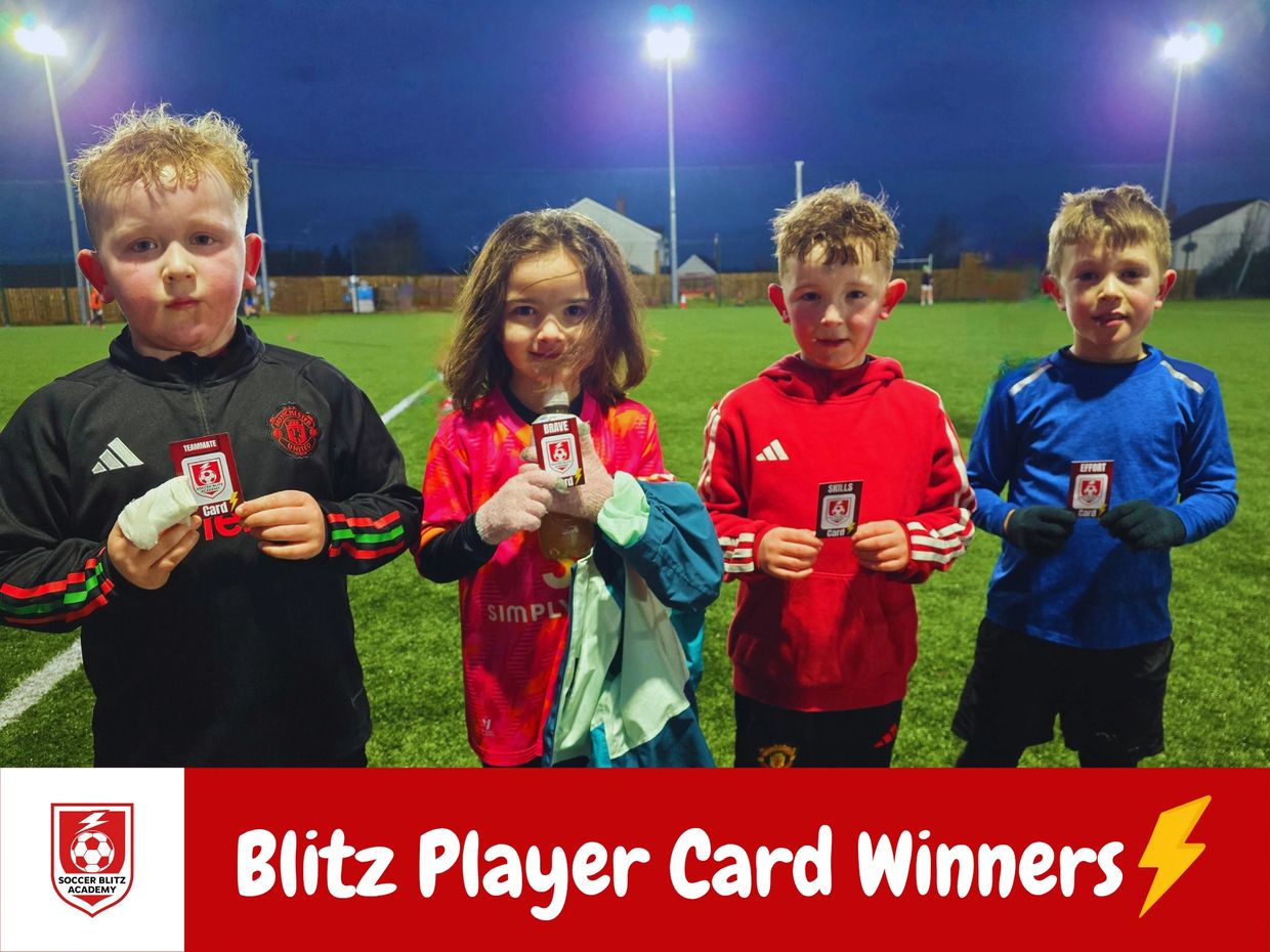 Four young soccer players proudly holding their Blitz Player Cards after a game.