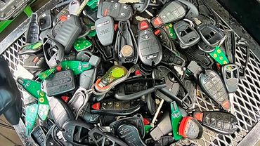A pile of various car key fobs and remotes on a metal surface.