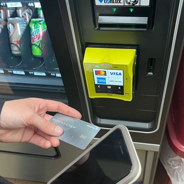 Hand holding credit card and phone in front of a vending machine.