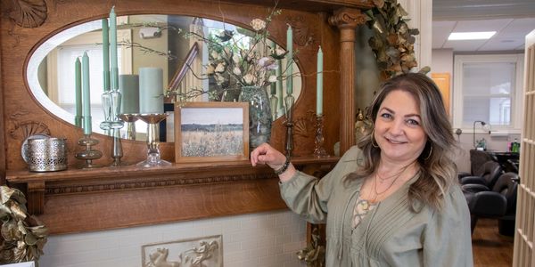 Woman smiling by a decorated wooden mantel with candles and flowers.