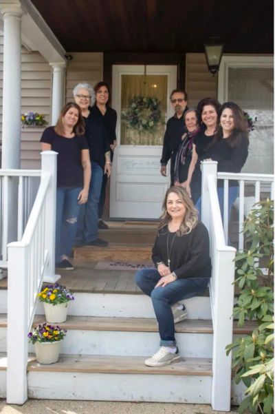 Group of people posing on a front porch with flower pots and a wreath on the door.