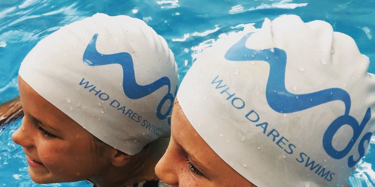 Two swimmers with water droplets on caps in a pool.