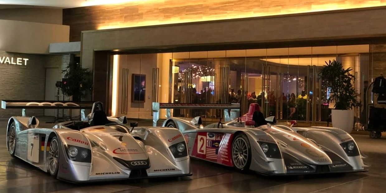 Two vintage Audi race cars displayed indoors with reflective floors.