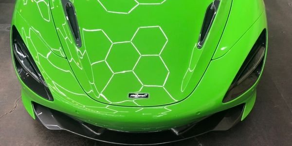 Green McLaren sports car hood with hexagonal light reflections.