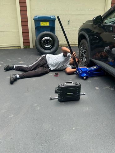 A man changing a car tire with tools and a jack on a driveway.