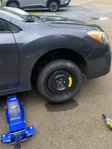 A car with a newly installed spare tire on the front wheel and a blue jack underneath.