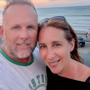 Smiling couple taking a selfie by the beach during sunset.