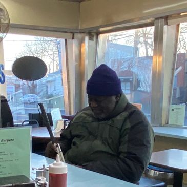 African American man sitting with a coat and hat at the counter
