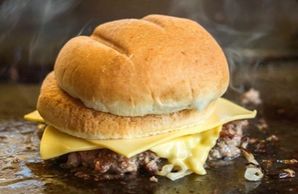 Hamburger with cheese, topped with a bun cooking on the grill.