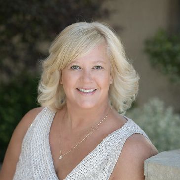 Smiling woman with blonde hair in a white sleeveless top outdoors.