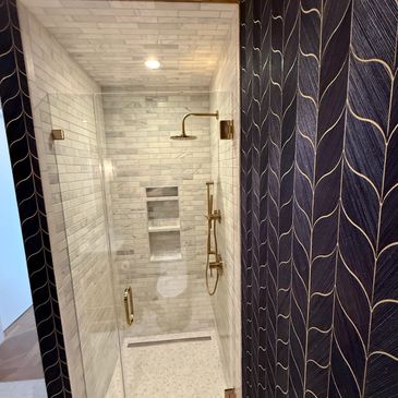 Modern bathroom shower with gold fixtures and patterned wall.