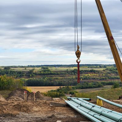 Crane hook hanging over construction site with pipes and countryside in background.