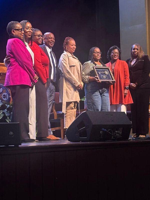 Group of people standing on stage, one holding a framed award.