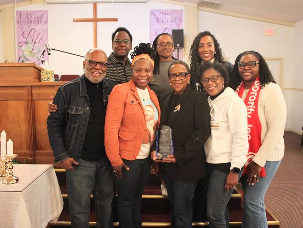 Group of eight people posing in a church, one holding an award.