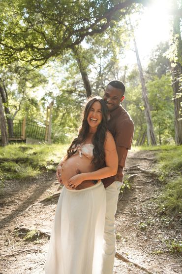 Happy couple embracing outdoors, celebrating pregnancy with smiles and sunlight.