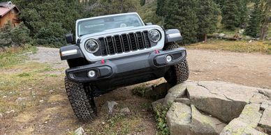 Gray Jeep Wrangler navigating over rocks on a dirt trail.