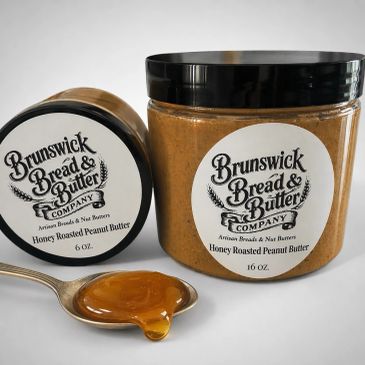 Two jars of Brunswick Bread & Butter Honey Roasted Peanut Butter with a spoonful of peanut butter.