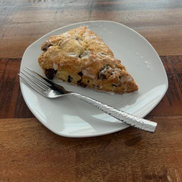 A slice of scone with chocolate chips on a white plate with a fork.