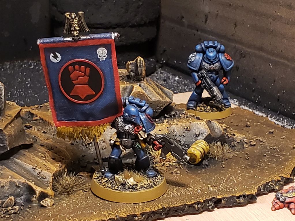 Two detailed blue Space Marine miniatures on a rocky battlefield base.