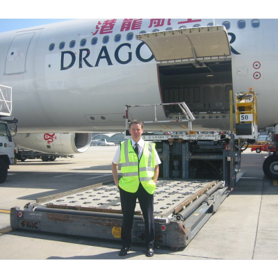 Man in high-visibility vest stands in front of a Dragonair airplane on the tarmac.