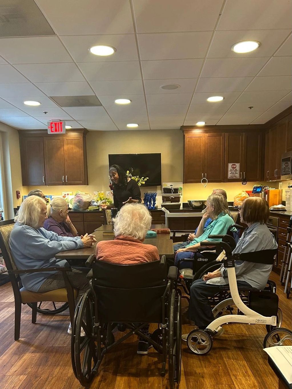 Elderly group in wheelchairs engaging with a caregiver in a room.