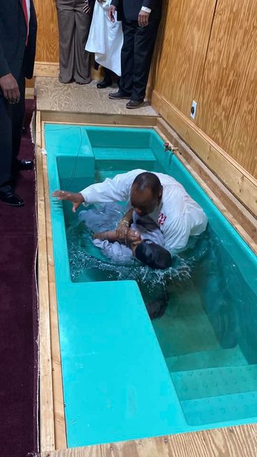 A man baptizing another person in a small indoor pool.