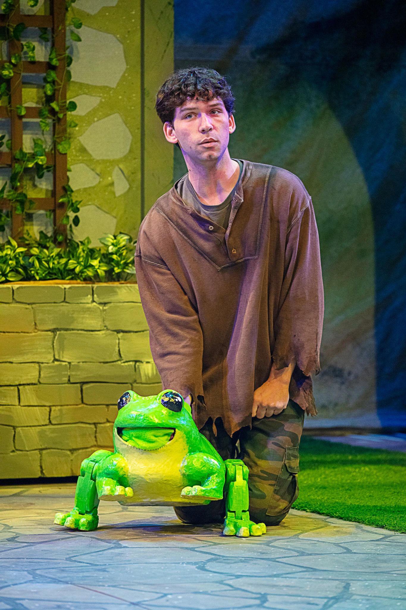 Actor kneeling with a large frog puppet on stage.