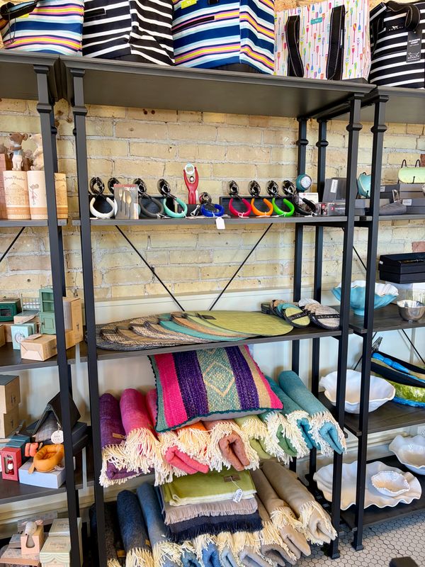 Colorful rolled blankets and pillow on a black metal shelf in a store.