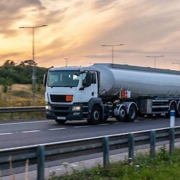 A white tanker truck driving on a highway at sunset.