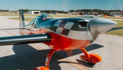 A person sits inside a small, sleek red and silver airplane on a runway.