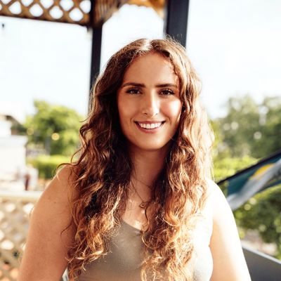 Smiling woman with long curly hair standing outdoors in natural light.