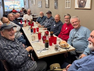 Group of elderly men enjoying a meal together at a long table.
