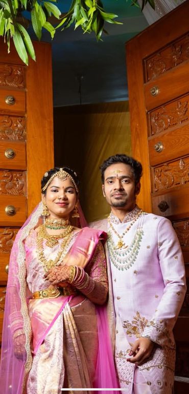 Indian couple in traditional wedding attire posing by wooden doors.