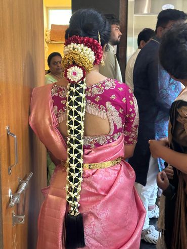 Woman in pink saree with intricate floral hair decoration at a traditional event.