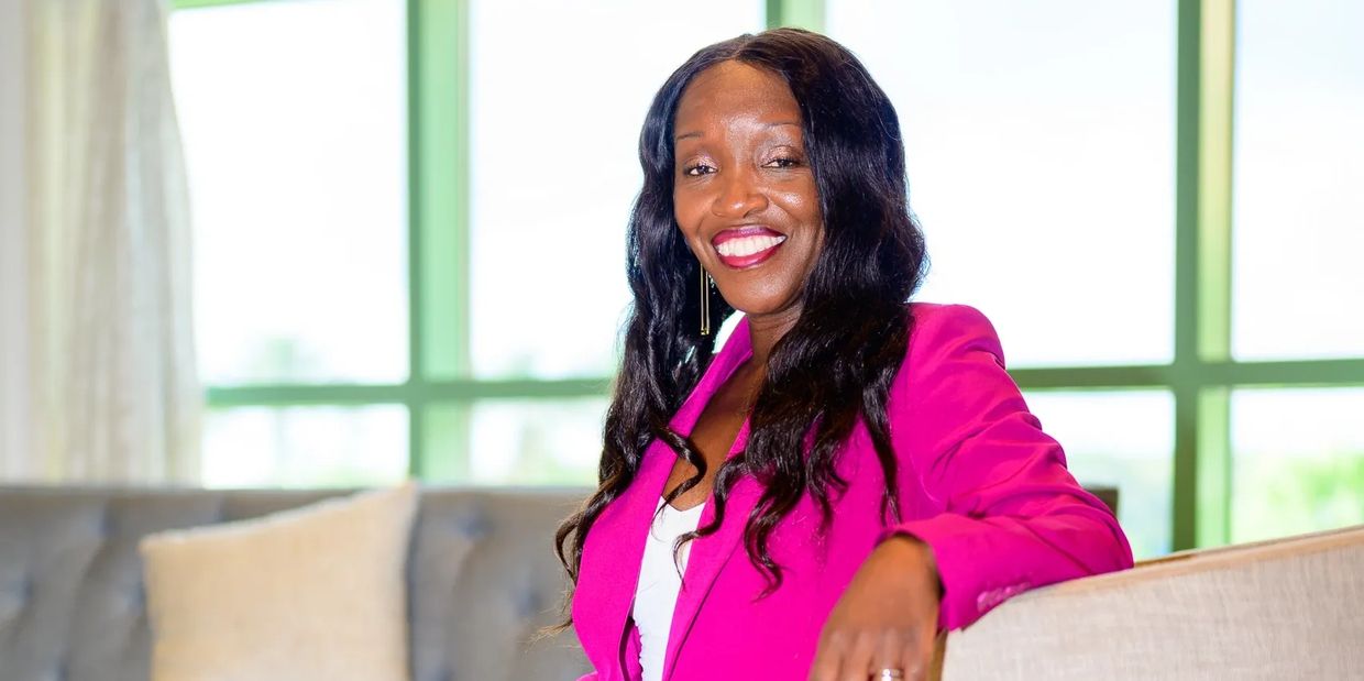 Woman in a bright pink blazer smiling indoors.