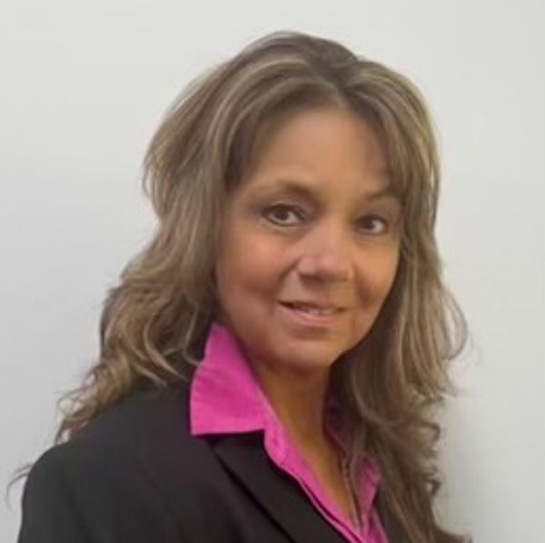 Professional woman in a black blazer and pink shirt smiling.