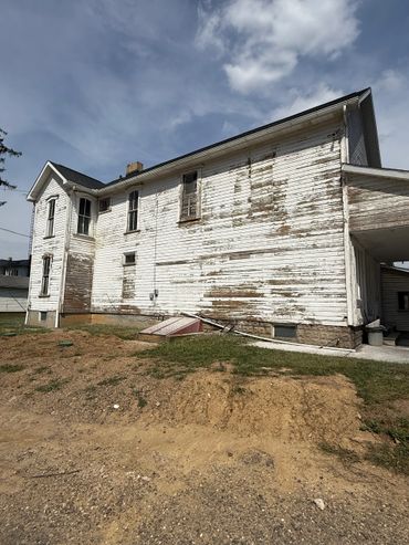 Old white wooden house with peeling paint under a cloudy sky.