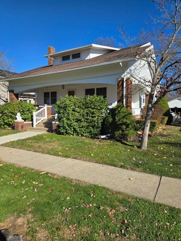 Cozy white house with a brown roof and lush green bushes under a clear blue sky.