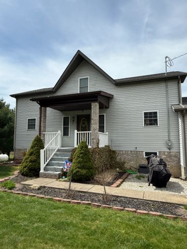 Gray two-story house with a small porch and trimmed bushes in front.