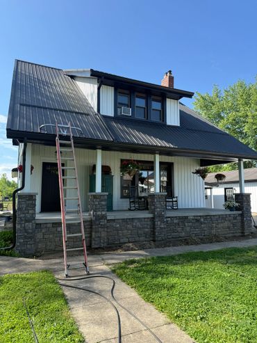 Front view of a house with a ladder on the porch and rocking chairs.